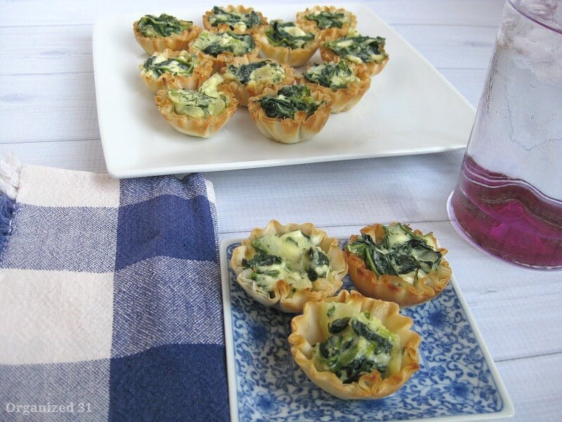 blue and white plate with 3 small spinach tarts on white wood table with blue and white napkin