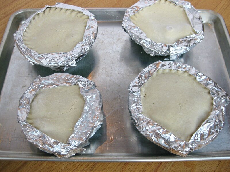 4 pot pies with crusts covered by foil on baking sheet