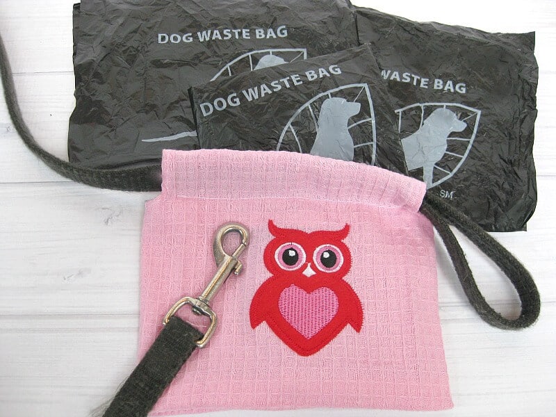 black dog waste bags next to pink DIY dog poop bag holder and leash