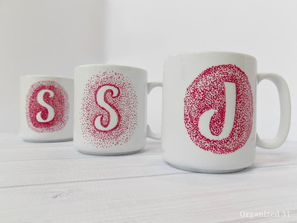 3 white and red monogrammed coffee mugs on white wood table