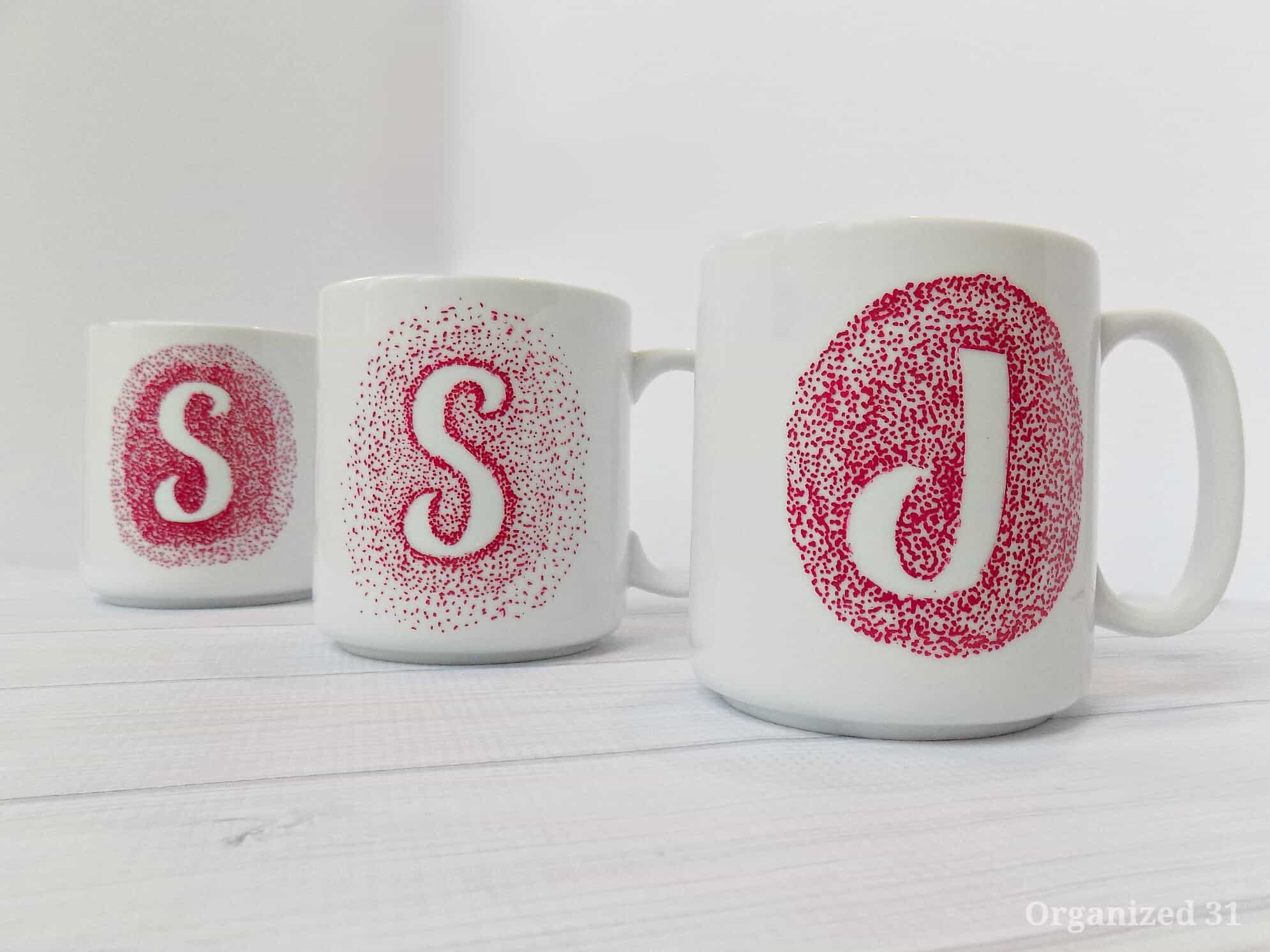three white mugs with lots of small red sharpie dots making initials.