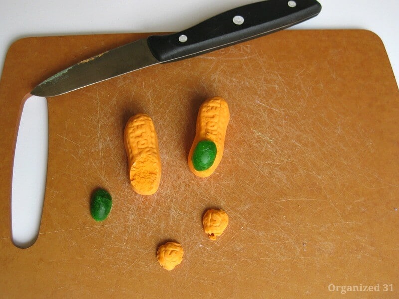 orange circus peanuts candy with top but off and half of green jelly bean on top of one to look like an orange finger with a green nail all on wood cutting board with knife