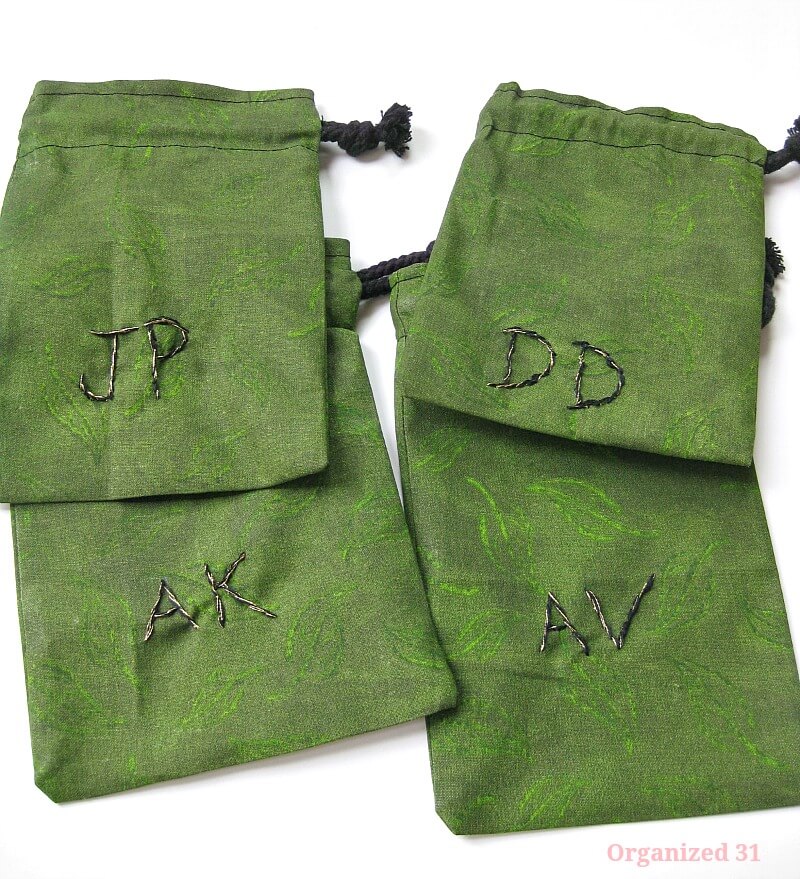 4 green cloth drawstring bags with black and gold embroidered initials