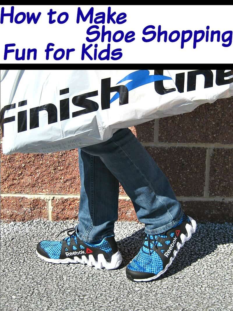close up of blue and black tennis shoes on person wearing jeans and carrying white Finish Line shopping bag in front of brick wall