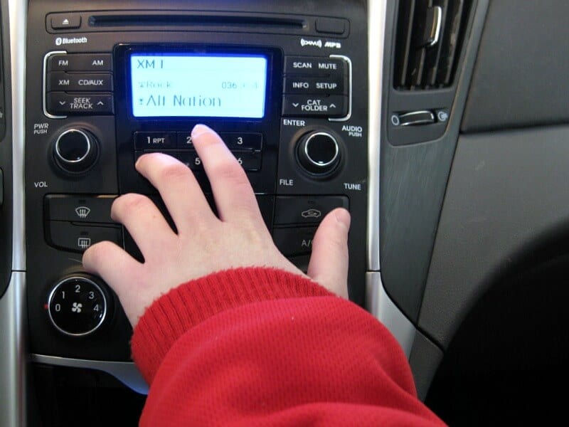 Child's hand  and red sleeve reaching for car radio button