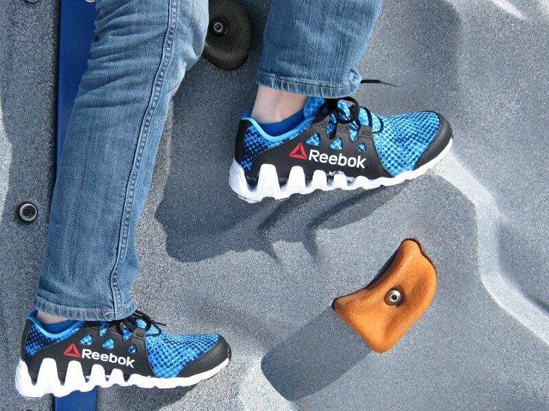 close up of blue and black Reebok tennis shoes on climbing wall