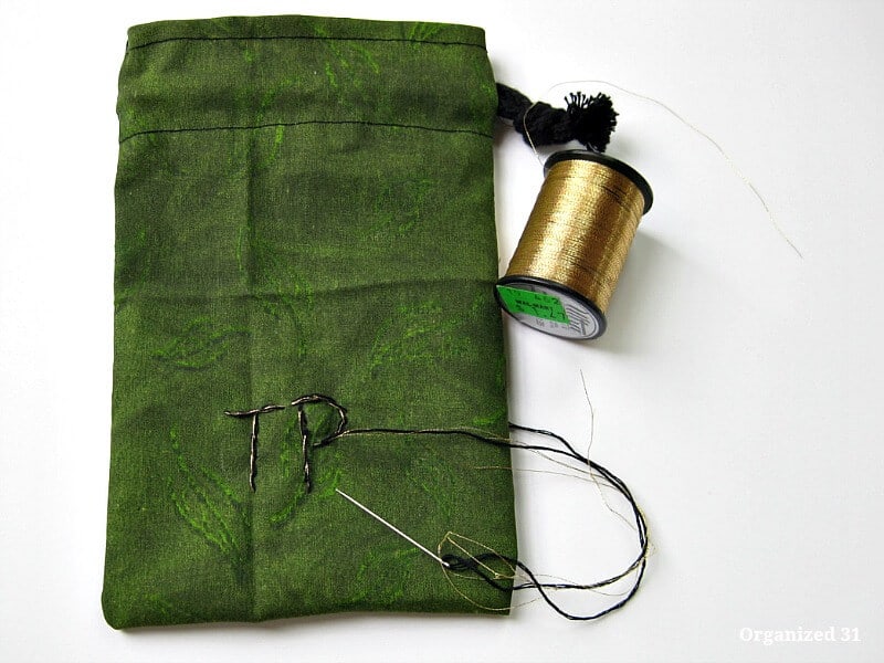 Green cloth drawstring bag with spool of gold thread and needle embroidering initials