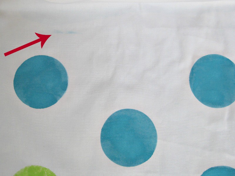 3 blue polka dots on white fabric with red arrow overlay pointing to smudge of blue paint
