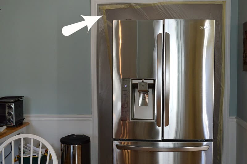 stainless steel refrigerator sitting in doorway with black arrow overlay pointing to corner of doorway