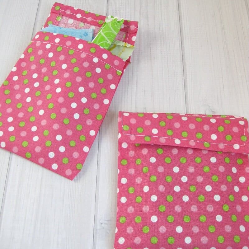 2 DIY pink fabric with green and white polka dots pouches with one  holding tampons on white wood table