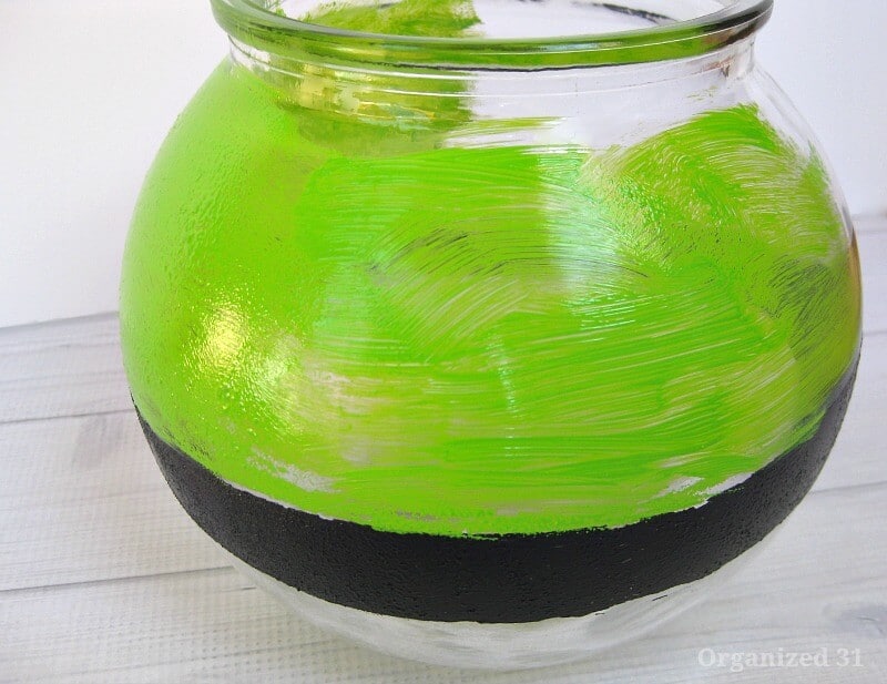 close up of round glass bowl with black painted stripe and green paint being painted on