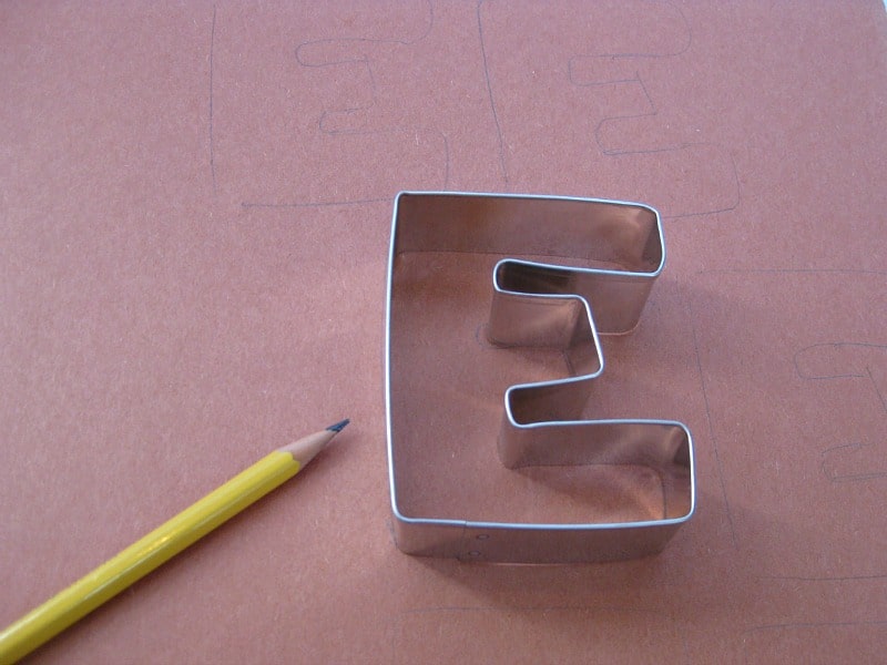 pencil, letter "E" cookie cutter on top of brown construction paper