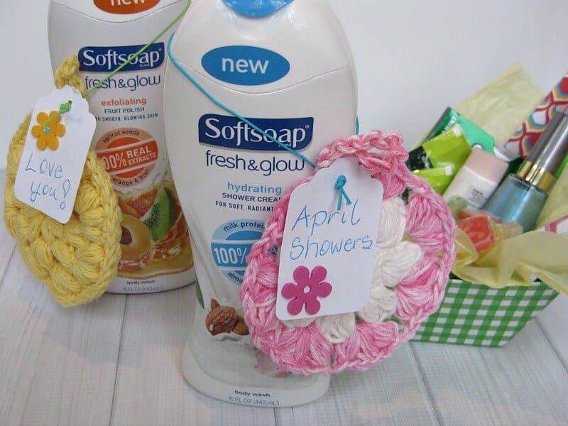 2 white bottles of body wash with crocheted pastel scrub sponges and gift basket in the background