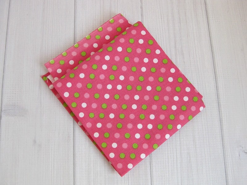 close up of folded pink fabric with green and white polka dots on white wood table