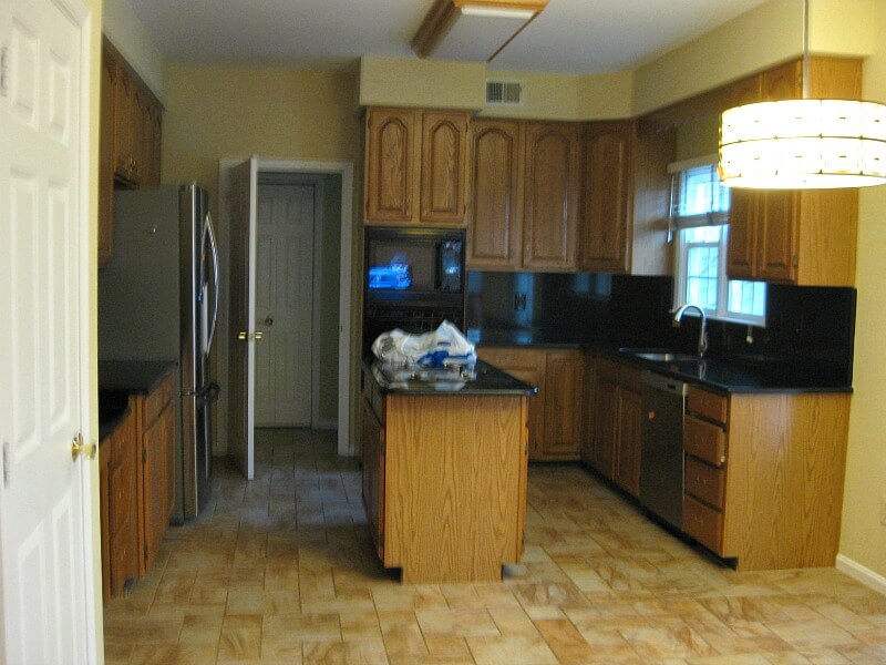 dark outdated kitchen with brown cabinets, black counters and brown tile floor