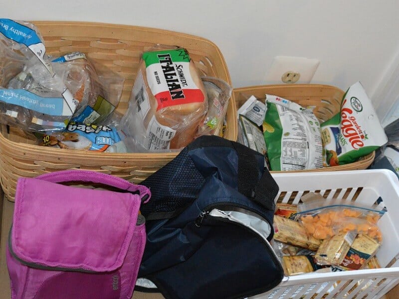 2 insulate lunch bags next to 2 baskets filled with lunch items, bread, bags of chips and packages of crackers