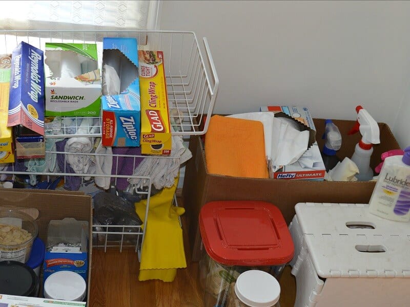 wire rack with kitchen bags and wraps and folded cloths next to box of cleaning supplies and white step stool
