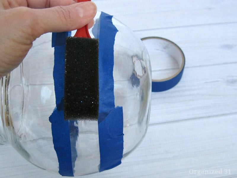 hand painting black paint onto  glass bowl with blue painters table making a stripe
