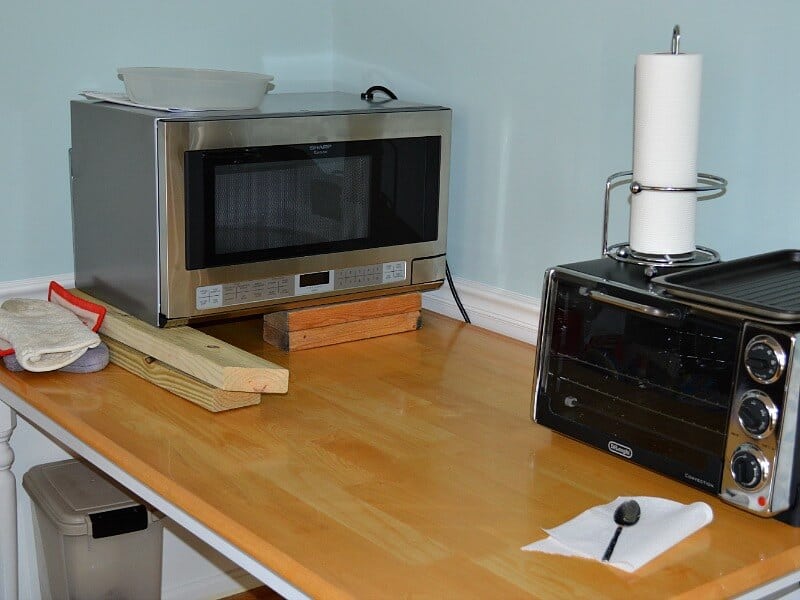 microwave sitting on 2 by 4 wood pieces and toaster oven set up on table