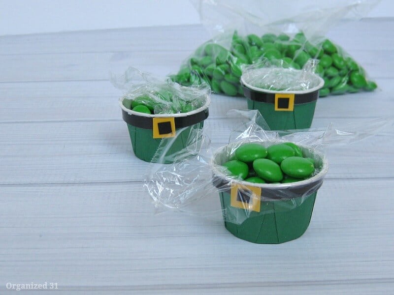 green cups with black belts and yellow buckles lined with plastic wrap and filled with green candies and back of green candies in the background