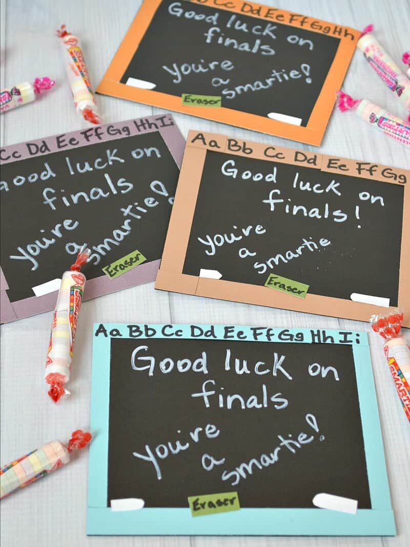 4 handcrafted card that looks like chalkboard that says "good luck on finals you're a smartie!" with candy and headache powder on white wood table