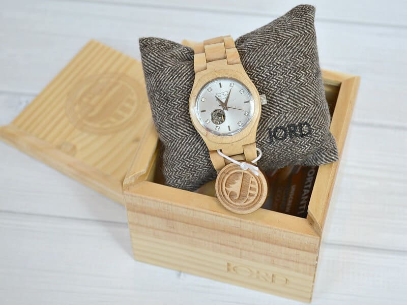 overhead view of wood watch on grey pillow inside of wood box on white wood table