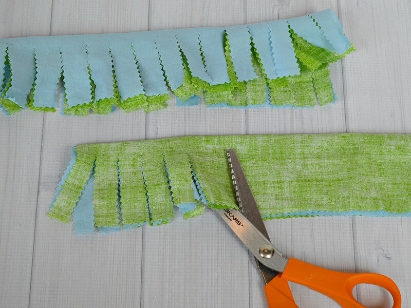 blue and green fabric with cut strips with orange handled pinking shears