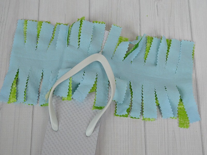 white rubber flip flop with blue and green fabric cut with fringes laid out