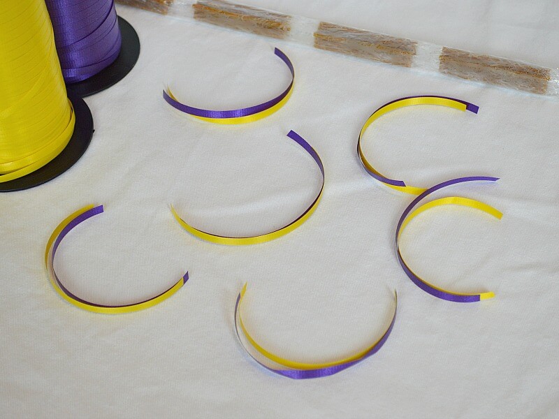 pieces of yellow and purple ribbon cut to same lengths next to line of dog treats wrapped in plastic wrap and roll of yellow ribbon and row of purple ribbon