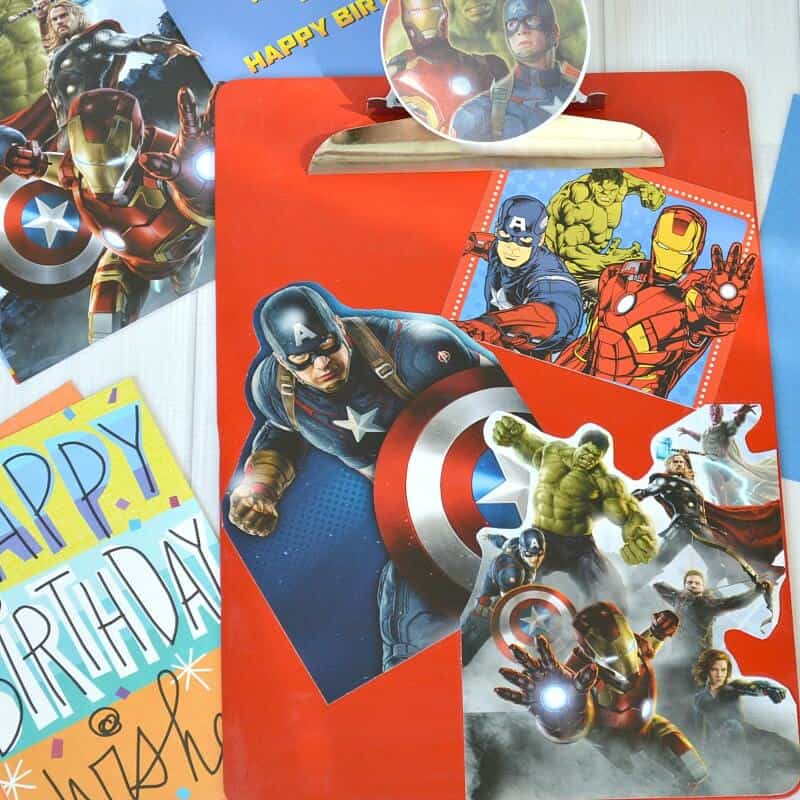 red clipboard with superhero images and cards scattered around on white table