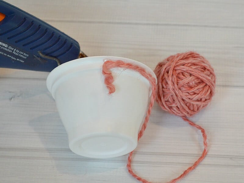 blue hot glue gun next to white pot with red yard being attached to pot