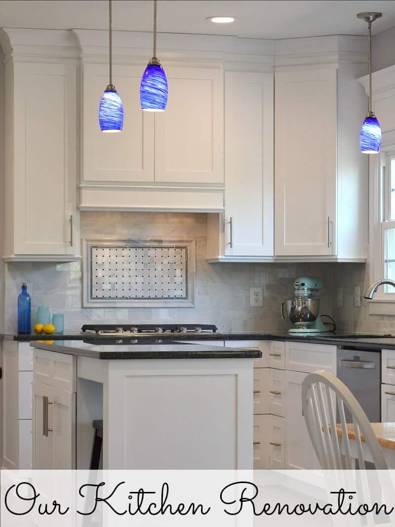 Modern white kitchen with black granite counters, white marble backsplash and blue hanging lights