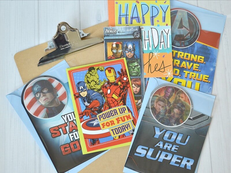 clipboard with 4 superhero cards, one happy birthday card and a package of superhero stickers on shite wood table