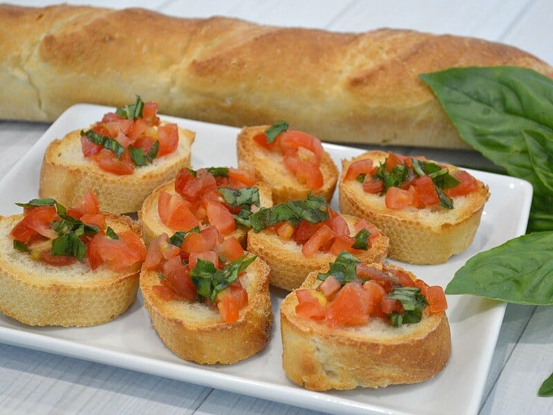 slices of bread on white plate with chopped tomato and basil leaves.