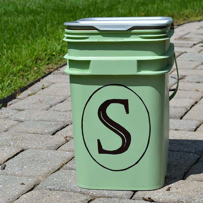 close up of black monogrammed letter S in black oval on green bucket sitting on brick path