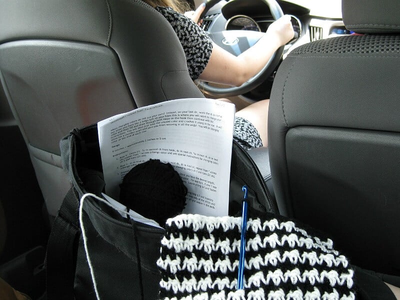 view from back seat of car at girl in black and white dress driving car and bag of black and white knitting
