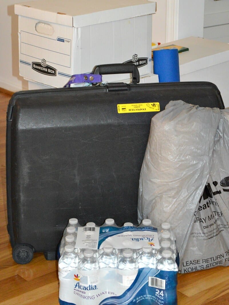 white boxes stacked with black suitcase, case of water and large plastic shopping bag on wood floor
