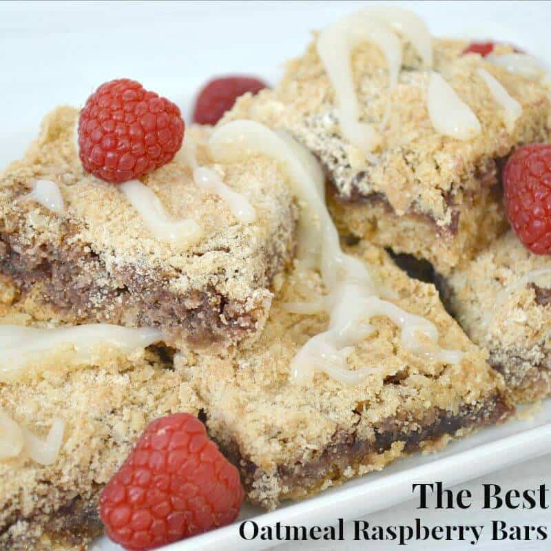 light brown baked bars with icing and fresh raspberries on white plate