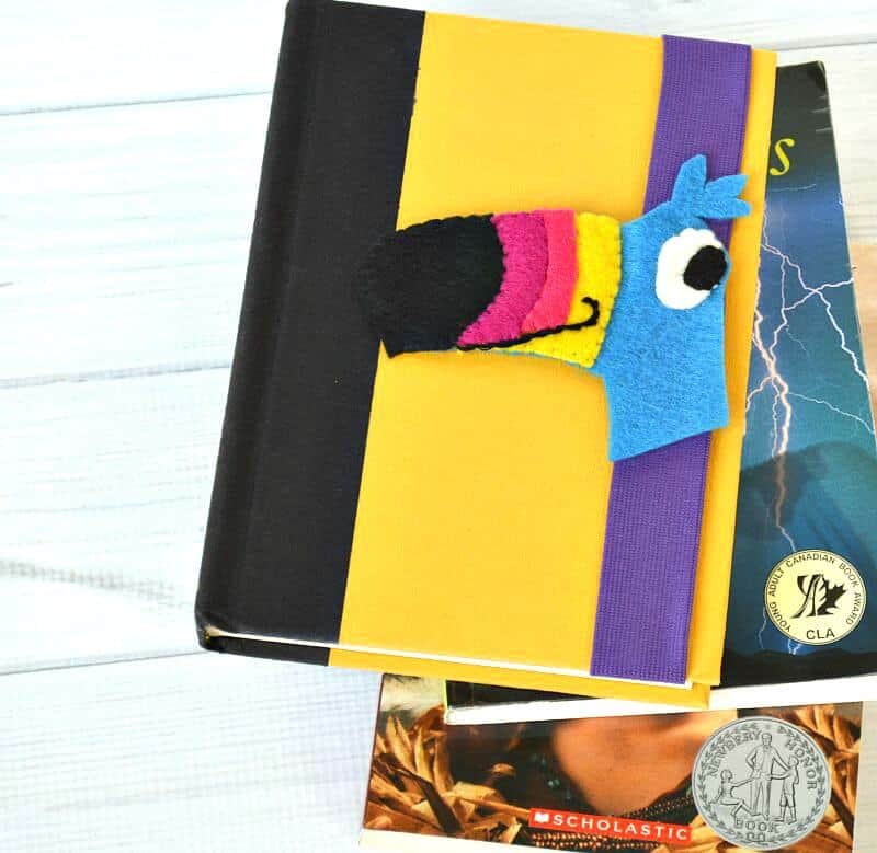 DIY felt book mark with toucan head on book with yellow cover and additional books underneath 
