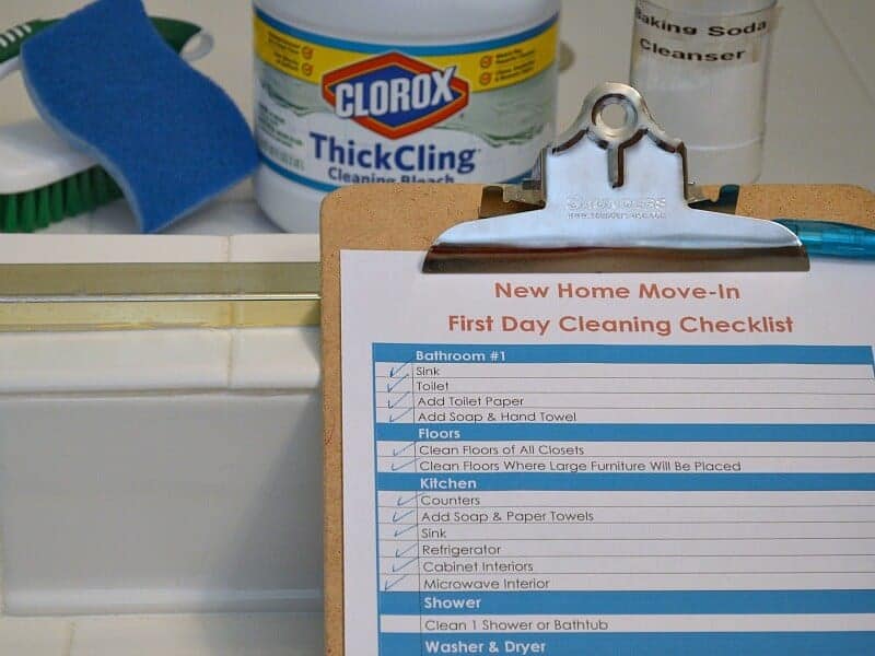 close up of clipboard with blue, red and white checklist and cleaning supplies in the background next to white tile shower