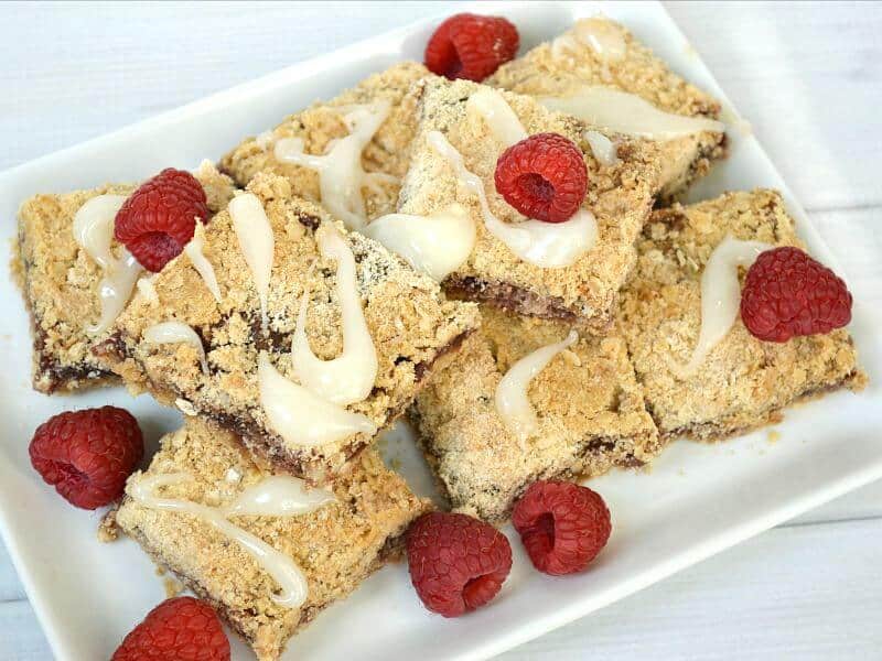overhead view of light brown baked bars with icing and fresh raspberries on white plate