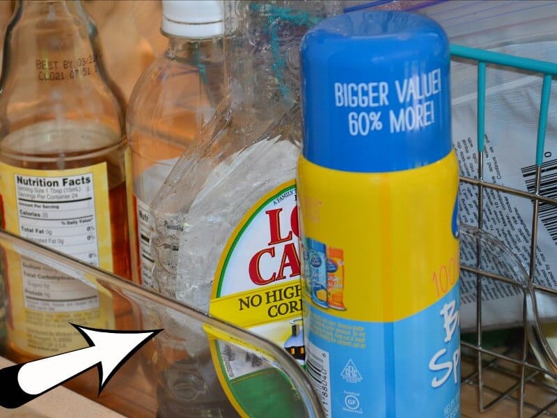 bottles of spray and syrup next to wire basket and clear container with white and black overlay arrow pointing to side of clear container.