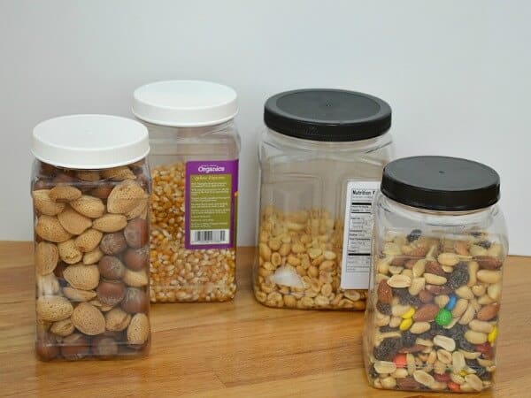 4 clear square canisters with nuts and snacks on wood table