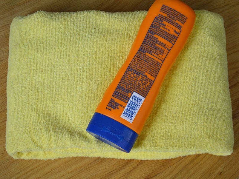 overhead view of orange bottle of sunscreen on folded yellow towel on wood table