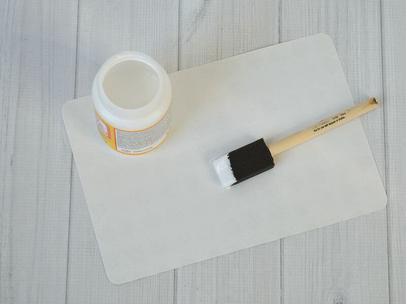 open jar of glue with sponge brush dipped in glue on table