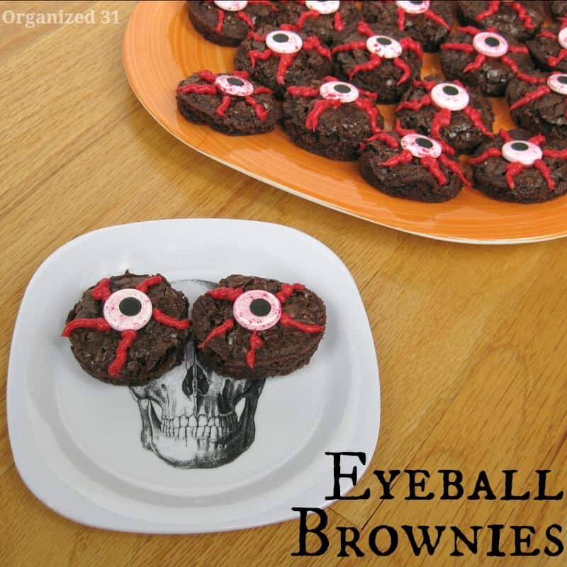 white plate with skull image and 2 round brownies that look like bloodshot eyes with large orange plate filled with eyeball brownies in background on wood table