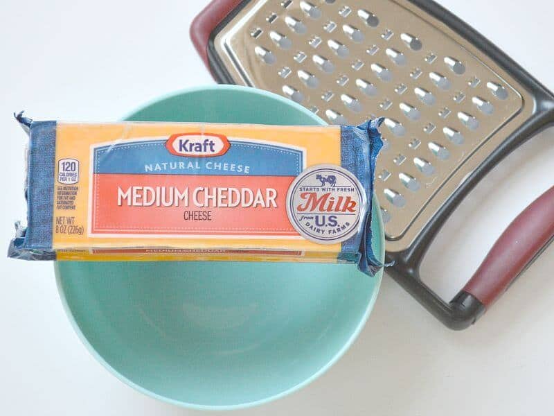 block of cheese in package on top of light blue bowl next to cheese grater