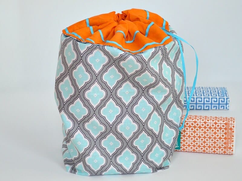 filled drawstring blue, grey and orange fabric bag with a blue and an orange package of tissues on white table