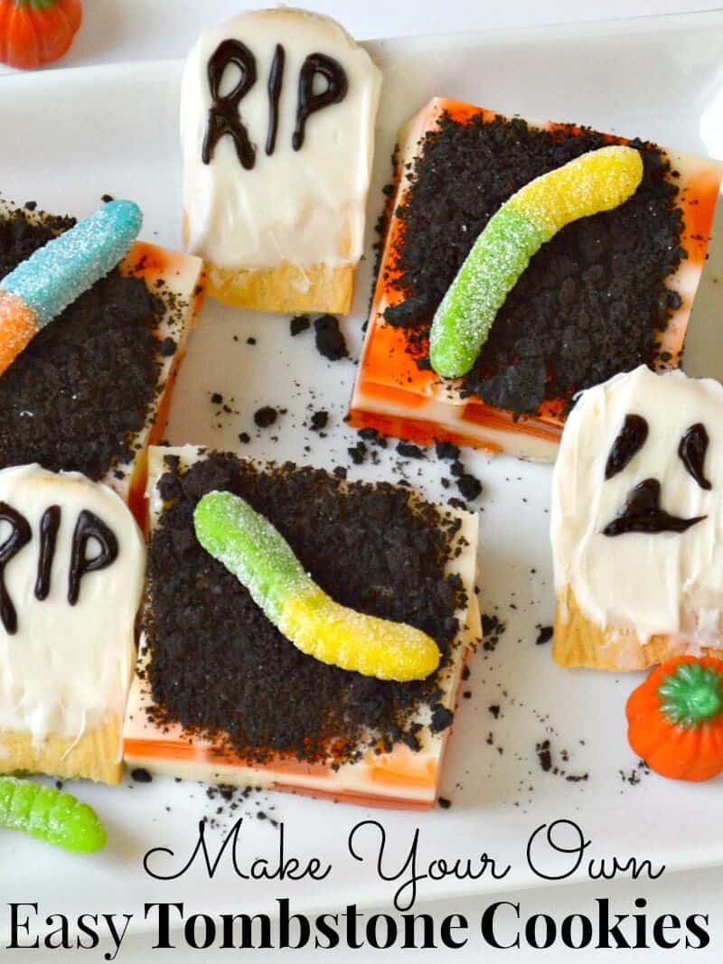 close up of iced cookies that look like ghosts and RIP tombstones with cubes of dessert with ground chocolate cookies and gummy worms