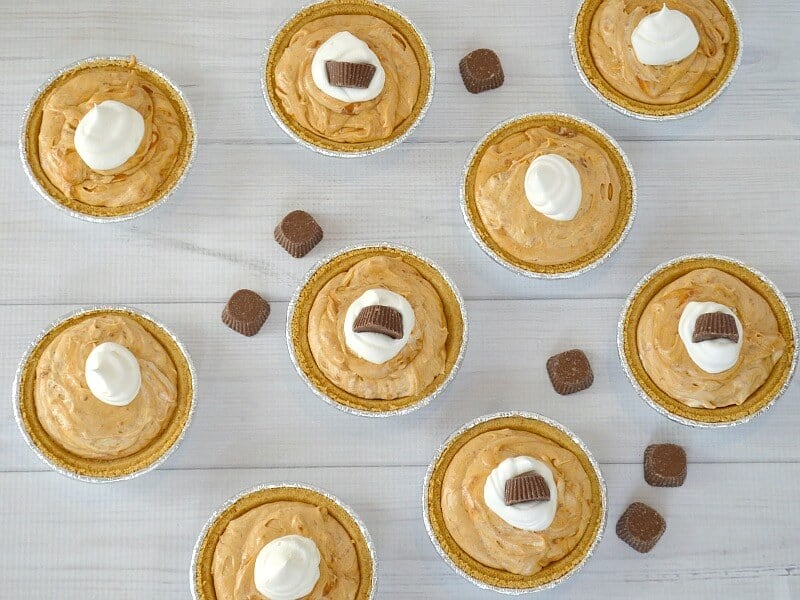 overhead view of mini pies with whipped cream and small chocolate candies on white table.
